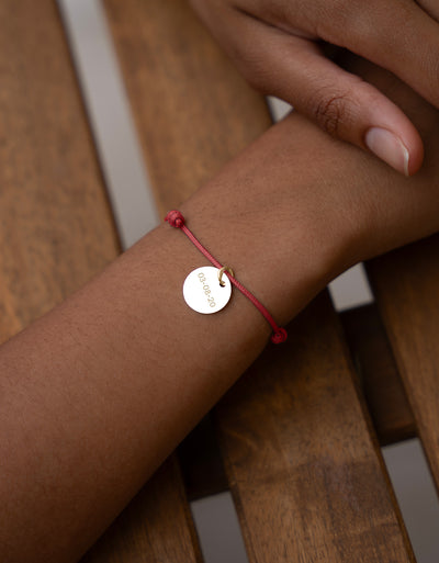 Un bracelet élégant avec une médaille de 15mm en plaqué or, personnalisée, sur cordon rouge.