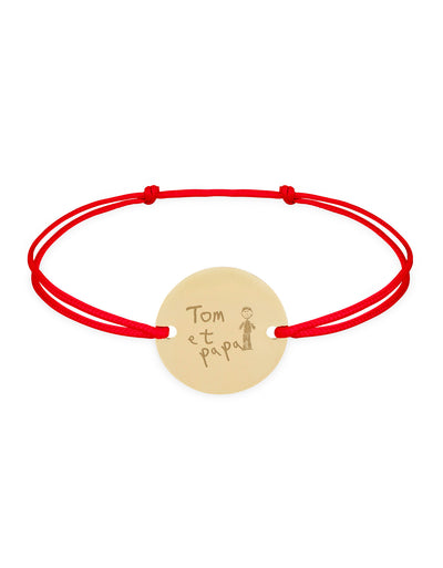 Un bracelet personnalisé, doté d'une médaille plaquée or de 15mm, accrochée par deux trous, sur cordon rouge.