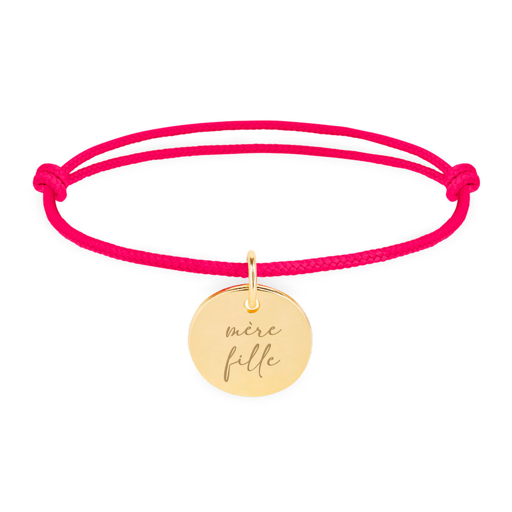 Un bracelet en plaqué or, orné d'une médaille de 15mm, complété par un cordon rose fuchsia.