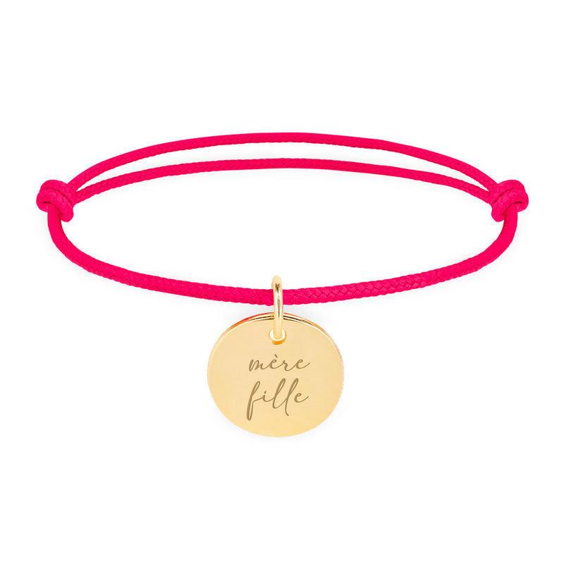 Un bracelet en plaqué or, orné d'une médaille de 15mm, complété par un cordon rose fuchsia.