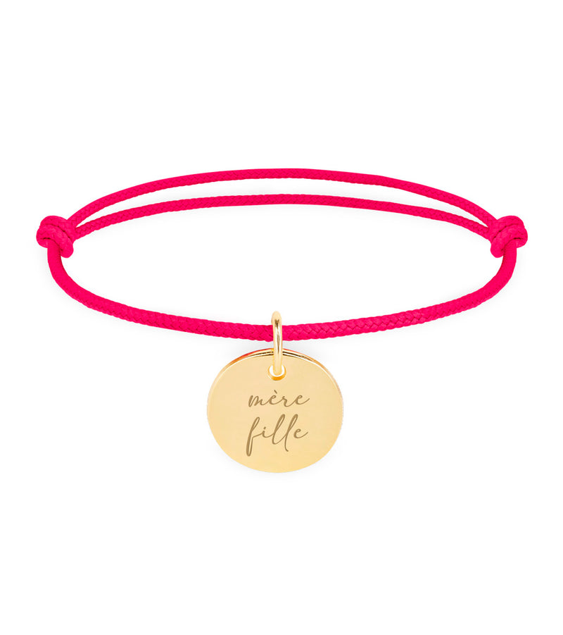 Un bracelet en plaqué or, orné d'une médaille de 15mm, complété par un cordon rose fuchsia.