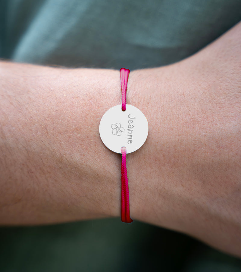 Un bracelet médaille, personnalisé en 20mm, agrémenté de deux trous en plaqué argent, ainsi qu'un cordon rose fushia.