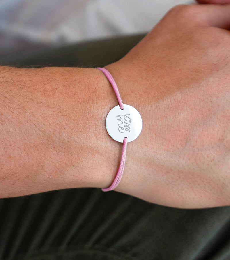 Ce bracelet, incluant une médaille personnalisée de 20mm, est orné de deux trous argent et d'un cordon rose élégant.