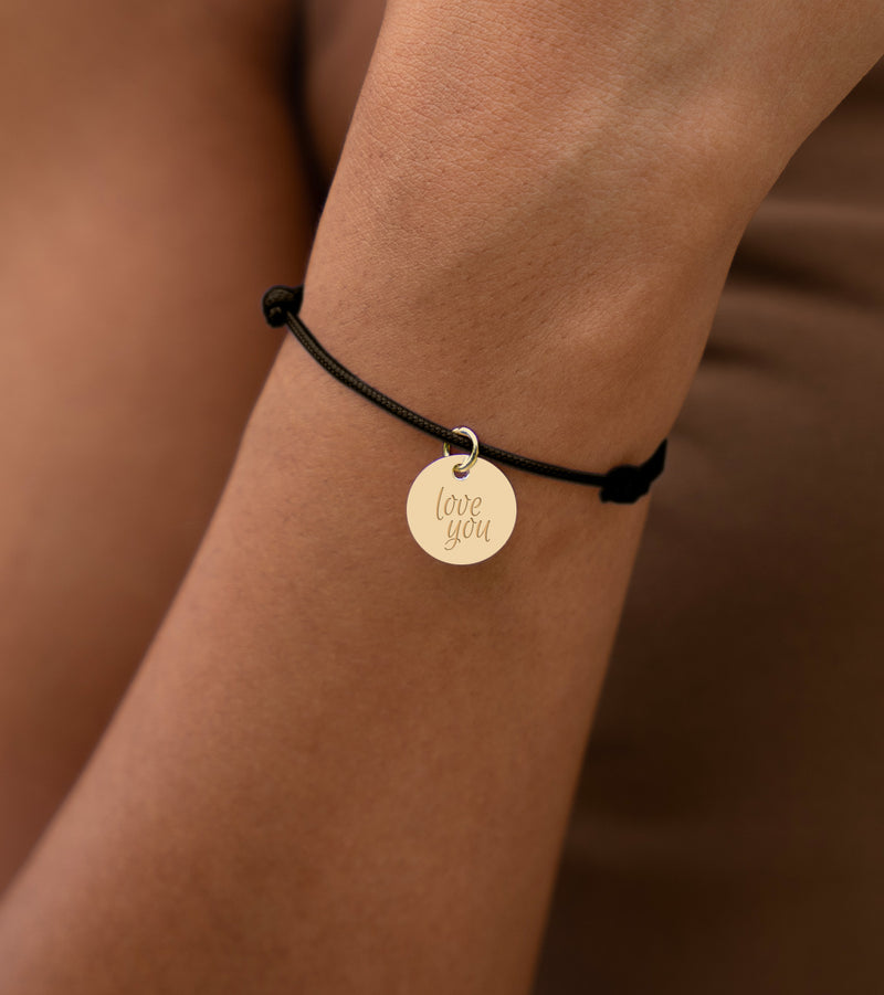 Bracelet unique en plaqué or, agrémenté d'une médaille de 15mm, attachée à un cordon noir.