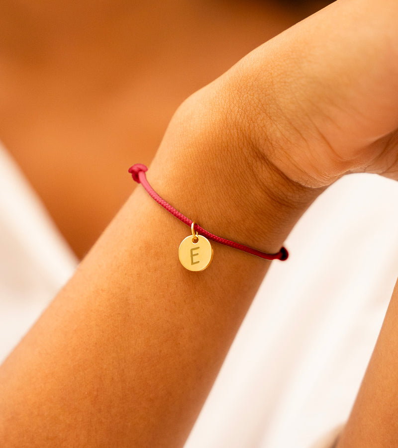 Une médaille plaquée or de 10mm sur un bracelet en cordon rouge, parfait pour afficher votre style avec sophistication.