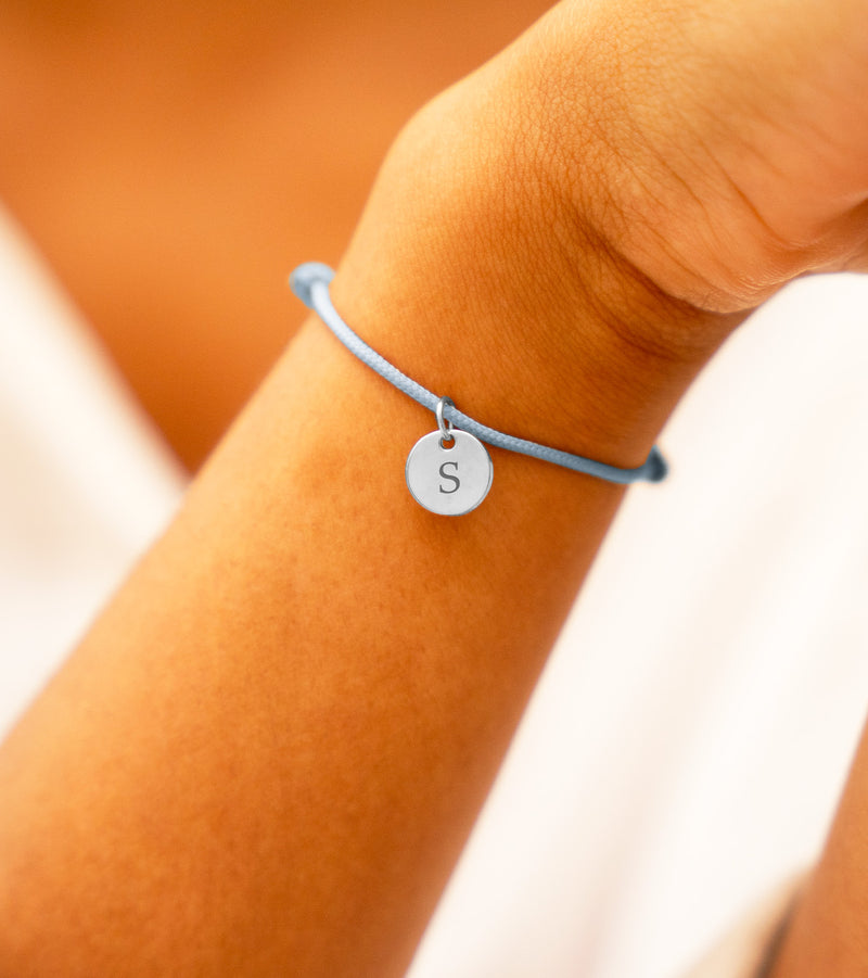 Cette image présente un bracelet personnalisé, avec une médaille en argent de 10mm sur un cordon de couleur bleu pastel.
