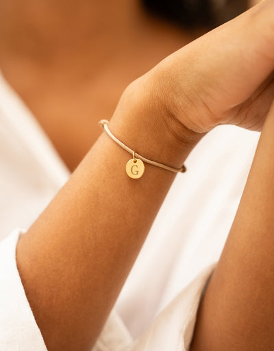 Bracelet cordon beige avec médaille plaquée or 10mm, un accessoire chic pour votre look quotidien.
