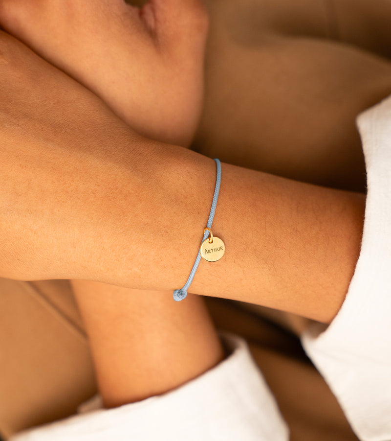 Un bracelet personnalisé en plaqué or, avec une médaille de 10mm, sur un cordon bleu pastel.