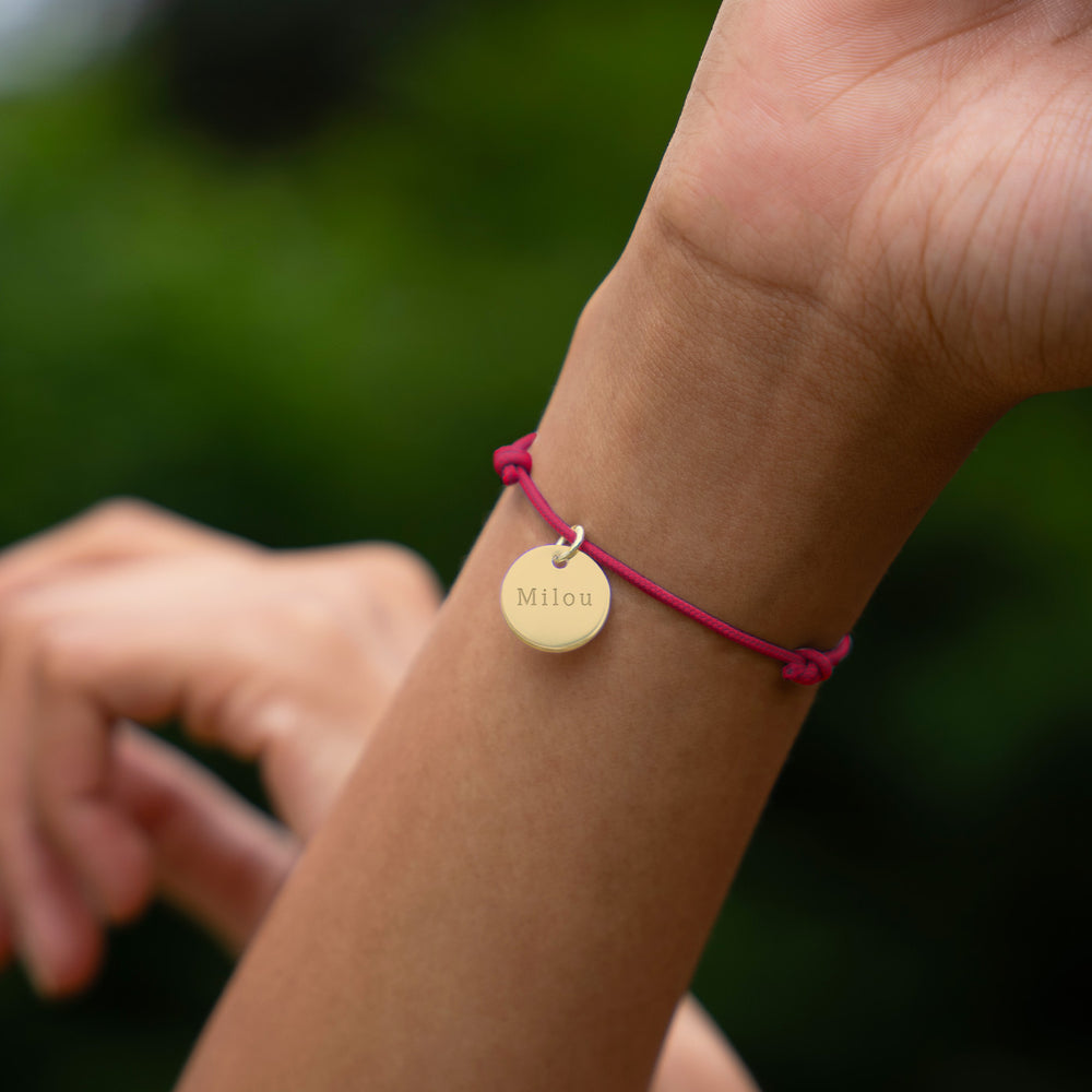 Un bracelet distingué, agrémenté d'une médaille de 15mm en plaqué or, sur un cordon rose fuchsia.