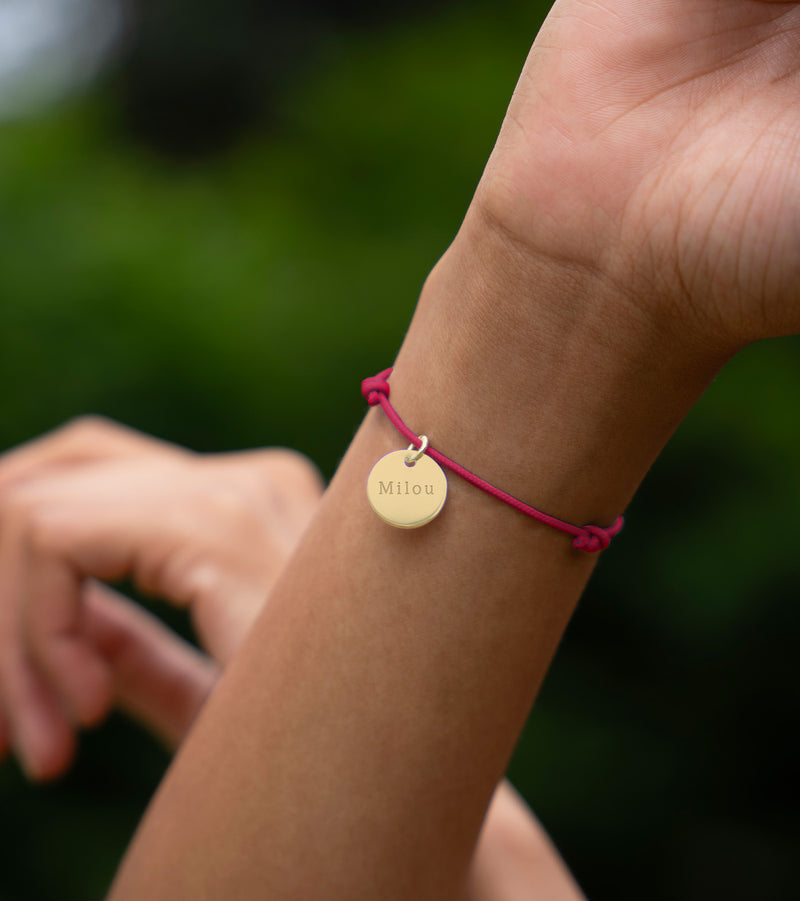 Un bracelet distingué, agrémenté d'une médaille de 15mm en plaqué or, sur un cordon rose fuchsia.