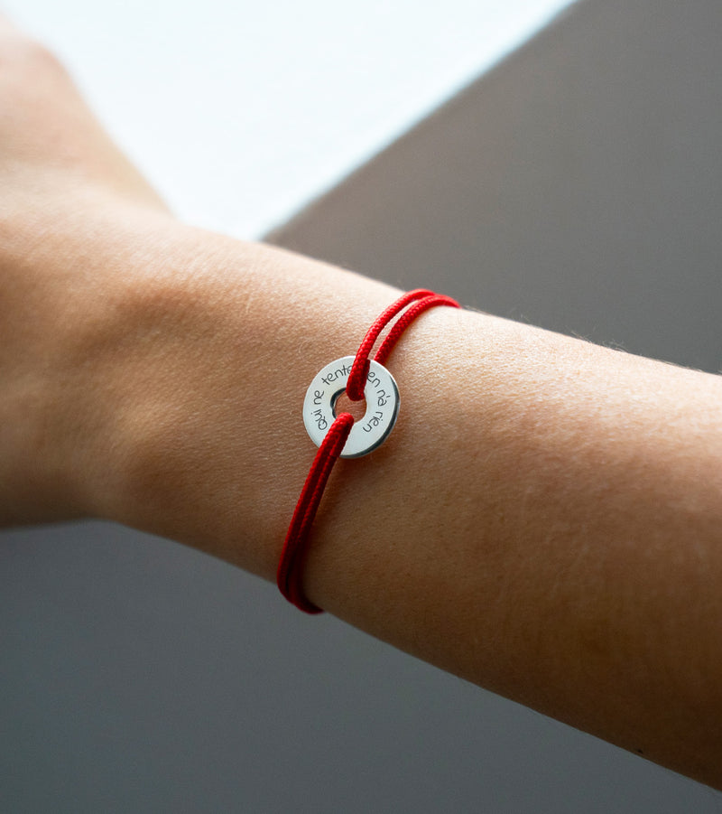 Arborant un cordon rouge, ce bracelet en forme de cible est personnalisé de 15mm en argent.