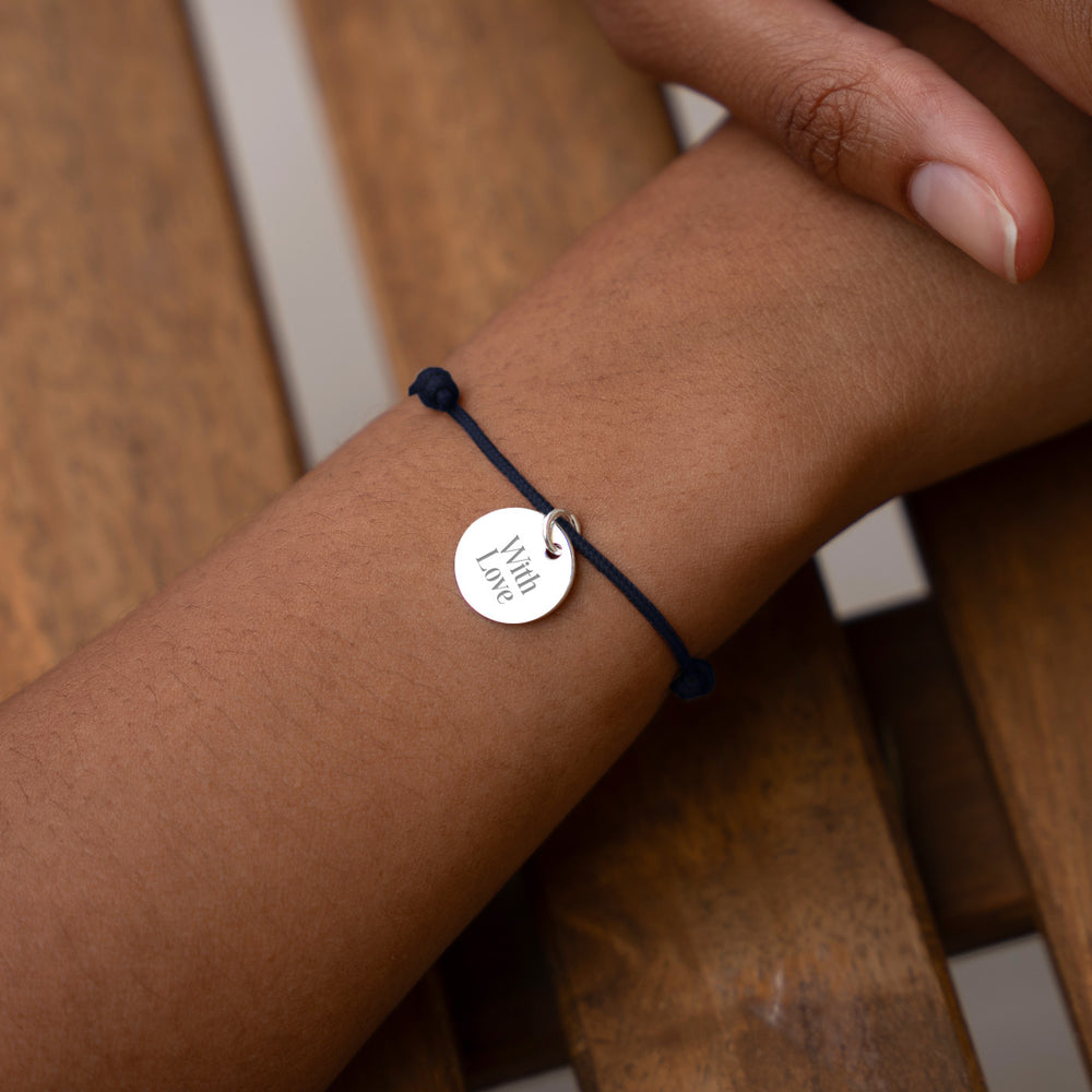 Un bracelet argenté avec une médaille de 15mm, accroché à un cordon bleu marine.