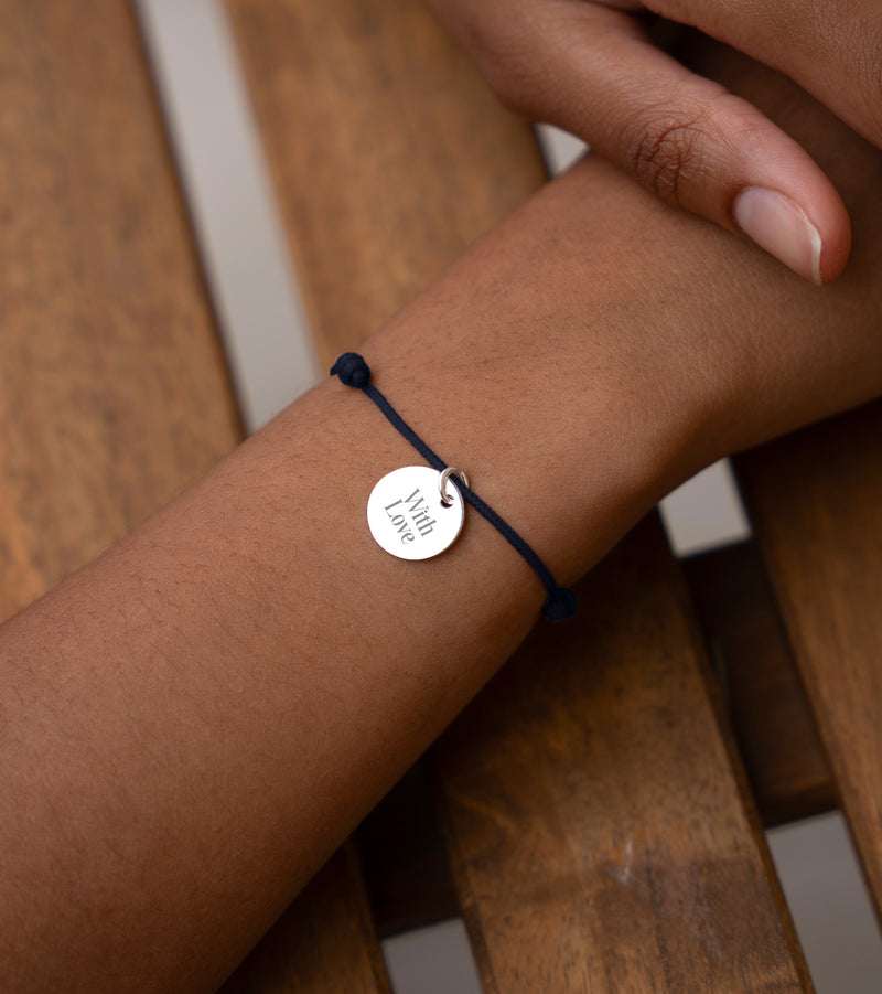 Un bracelet argenté avec une médaille de 15mm, accroché à un cordon bleu marine.